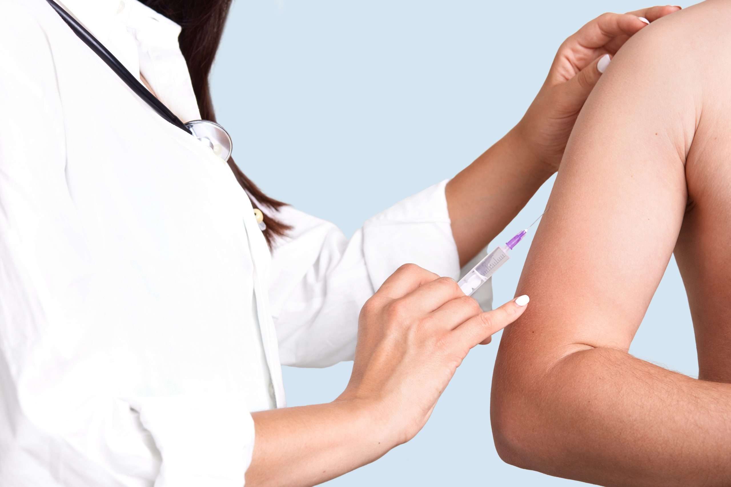 close up shot female doctor s hands makes vacciantion patient uses syringe inject upper arm prevents serious disease isolated blue wall selective focus heathcare concept scaled