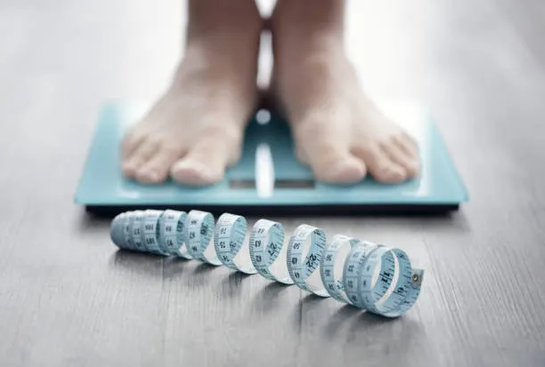 Bare feet on a bathroom scale beside a measuring tape