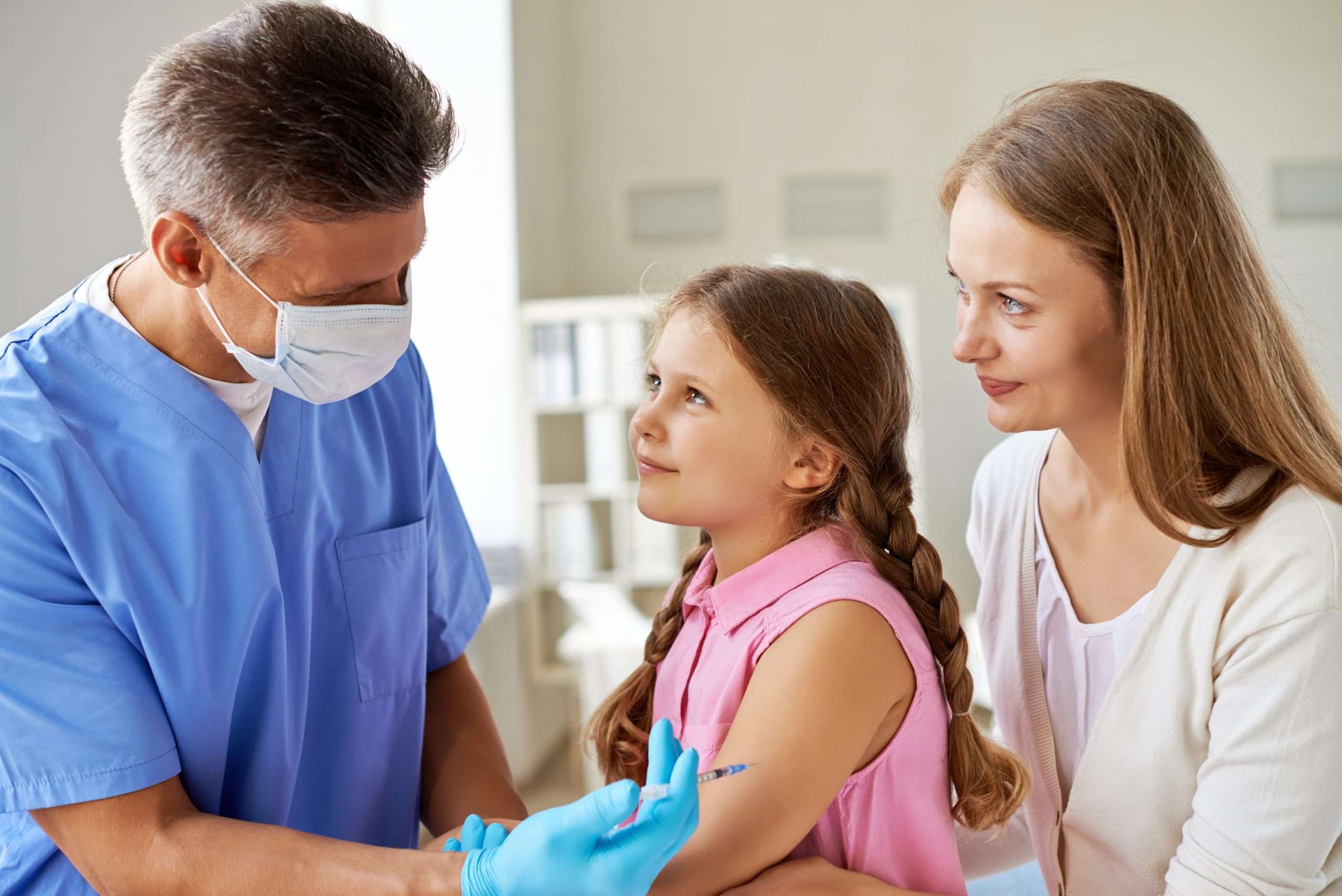 A physician vaccinates a young girl as her mother looks on